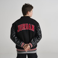 a young boy wearing a black jordan varsity jacket
